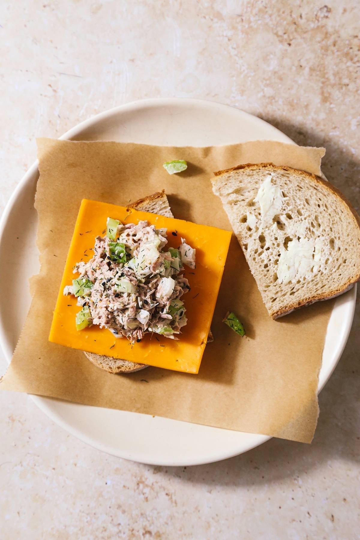 Open-faced air fryer tuna sandwich being assembled on a white plate with parchment paper.