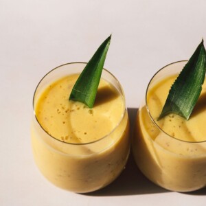 Image of two mango pineapple smoothies with a pineapple leaf garnish.