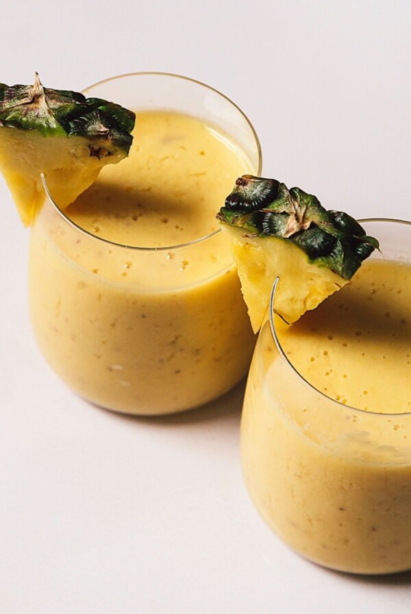 Close-up image of two mango pineapple smoothies with a pineapple garnish.