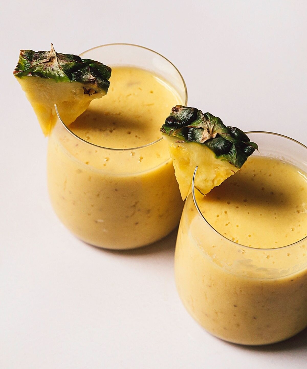 Close-up image of two mango pineapple smoothies with a pineapple garnish.