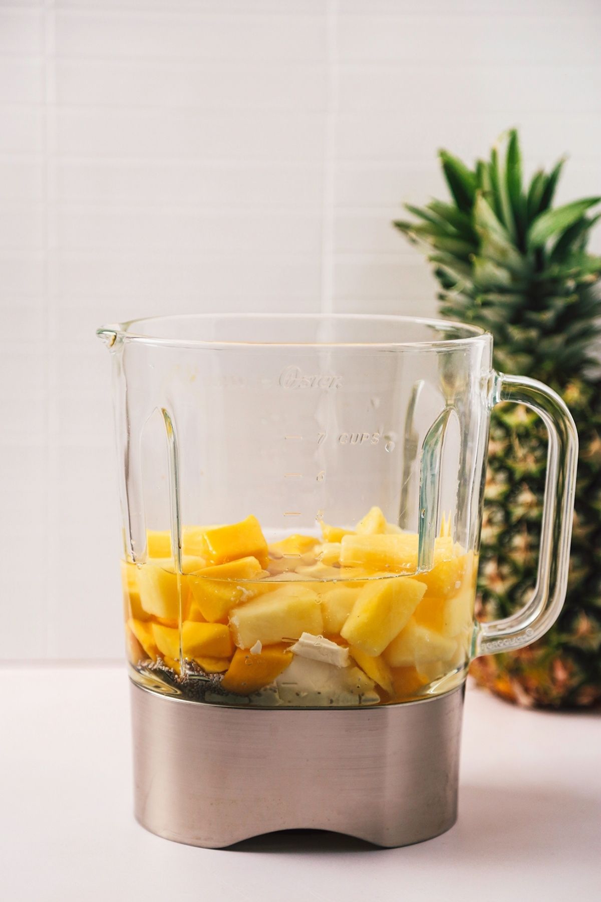 Mango pineapple smoothie recipe ingredients in a blender with a pineapple off to the right side.